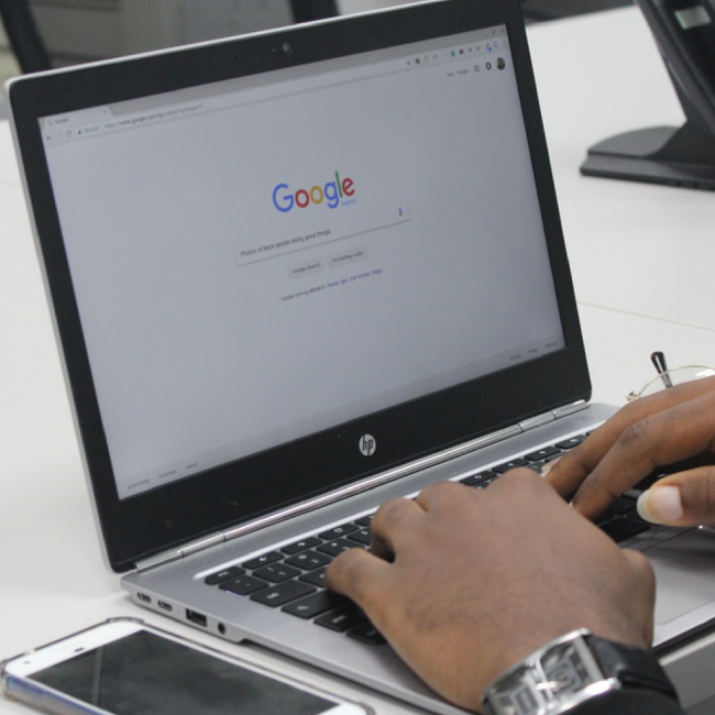 Laptop on desk with persons hands typing on keyboard and "Google" on the screen