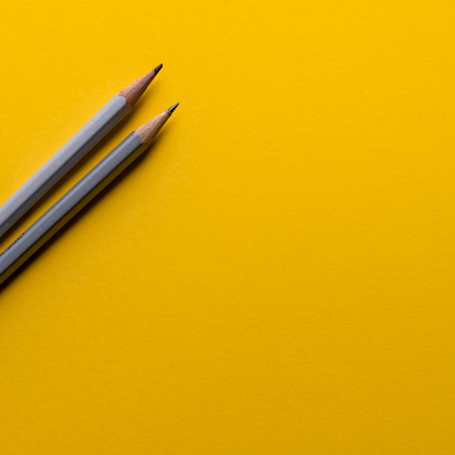 Two gray pencils for writing alt text for a website sitting on a yellow background